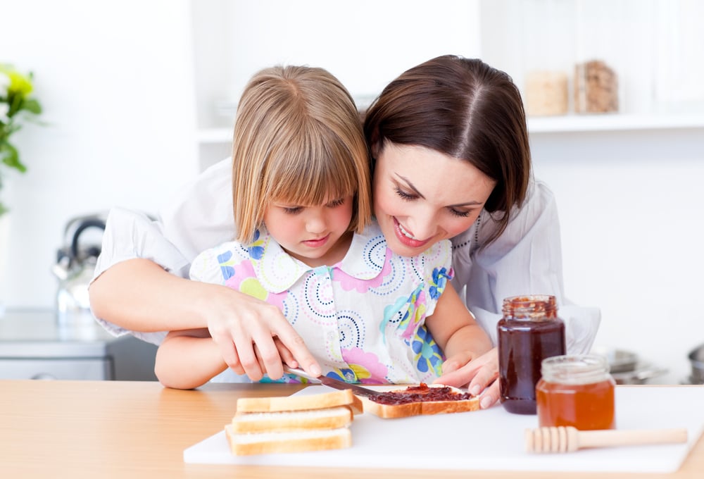 Affectionate mother helping her daughter prepare the breakfast in the kitchen