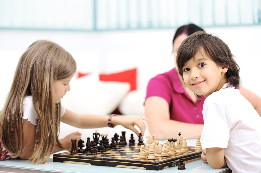 Brother and sister playing chess at home with their mother